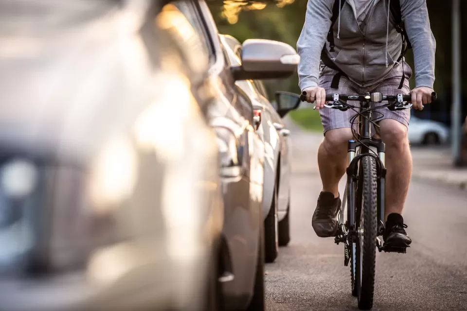 Man on bike rides next to parked cars.